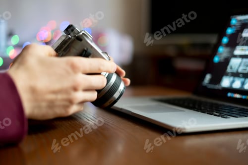 Preview: young male photographer holding a camera and prcessing his photos on laptop in the studio f