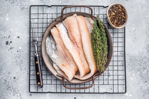 Preview: Raw Hake fish fillet in steel tray with herbs. grey background. top view