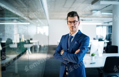 Preview: A portrait of young businessman standing in an office, arms crossed