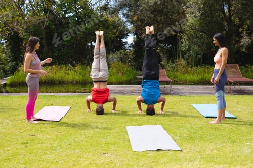 Preview: Full length of women looking at men practicing handstand in park on sunny day