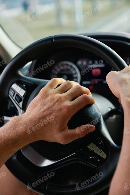 Preview: Close up of a person s hand gripping a steering wheel in a car interior with a focus on the