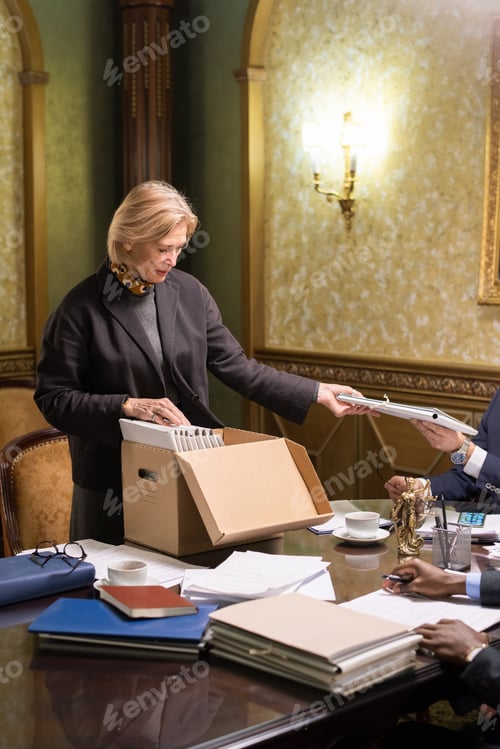 Preview: Blond mature businesswoman taking folder with papers from hand of colleague