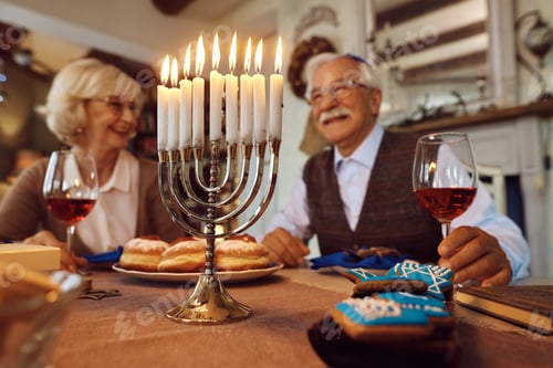 Preview: Close up of lit candles in menorah with happy senior Jewish couple in background.