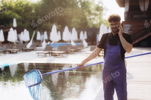 Preview: Pool cleaner holding leaf skimmer and talking on phone by the pool