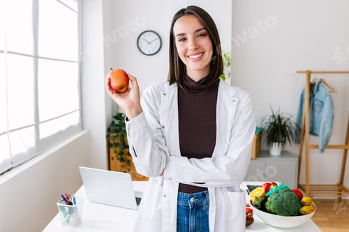 Preview: Portrait of young nutritionist woman holding red organic apple at medical office