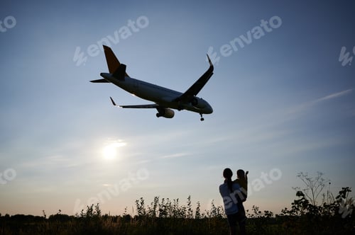 Preview: Silhouette of woman with child looking at landing commercial airplane