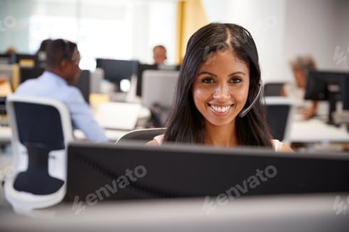 Preview: Young woman working at computer with headset in busy office