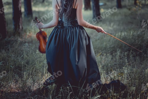 Preview: back view of woman in witch costume walking on forest, holding violin