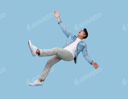 Preview: excited asian man relaxing floating in mid-air isolated on blue copy space background.