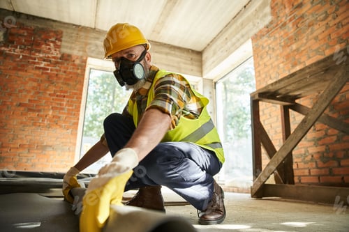 Preview: hardworking construction worker in safety helmet and gloves with dust mask putting carpet on floor