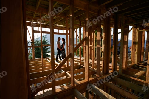 Preview: Man and woman inspecting their future wooden frame house nestled in the mountains near forest.