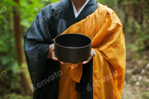 Preview: Close up of Buddhist monk wearing black and yellow robe, holding singing bowl.