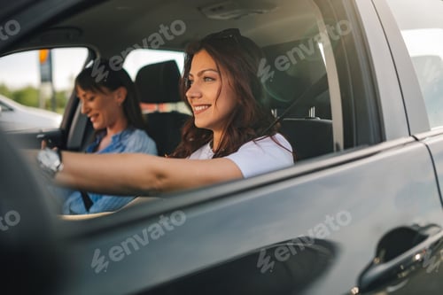 Preview: Cheerful young woman driving a car while her friend using a cellphone.