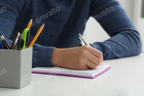 Preview: Man writing in notebook at white table indoors, closeup