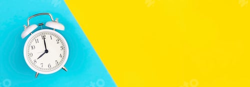 Preview: White alarm clock on a blue and yellow background, flat lay.