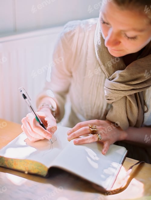 Preview: A woman using a coloured pen drawing on a blank page of a diary.