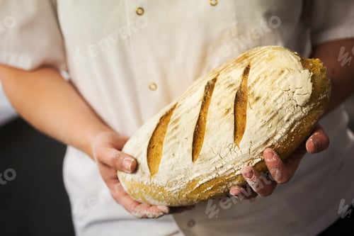 Preview: Close up of person holding a freshly baked laof of bread.