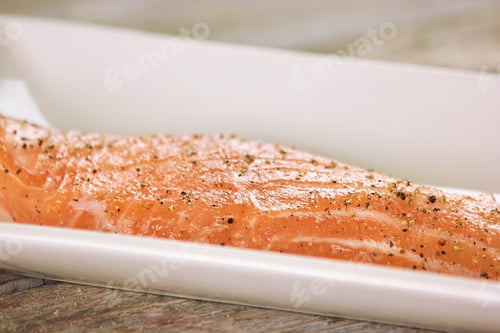 Vea de cerca el salmón crudo con pimienta en una olla rectangular.