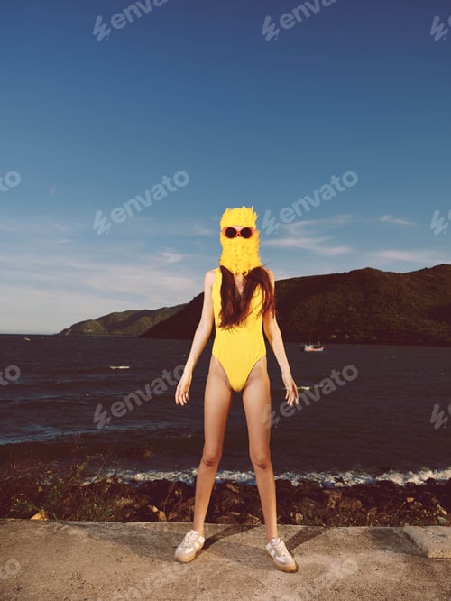 Preview: A woman in a yellow swimsuit and sunglasses stands by the roadside near a scenic body of water, with