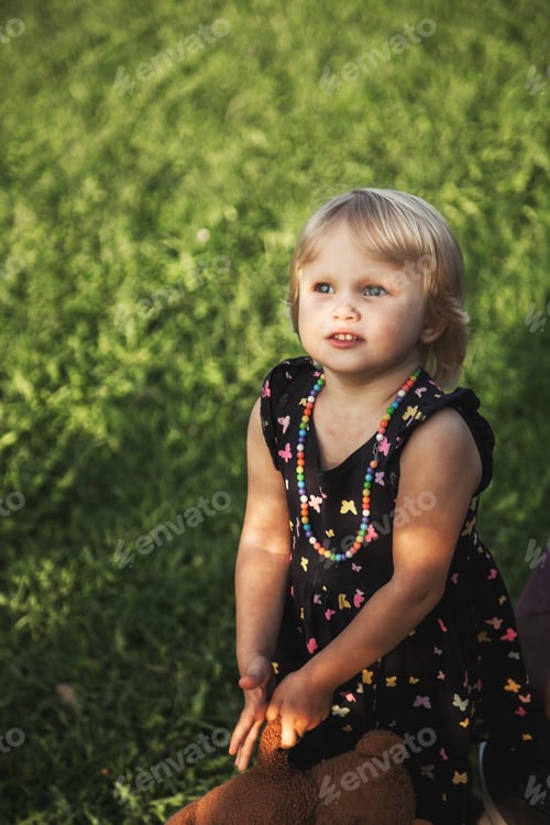 Preview: A cute two-year-old girl in a dress is having fun in a summer park on the green grass