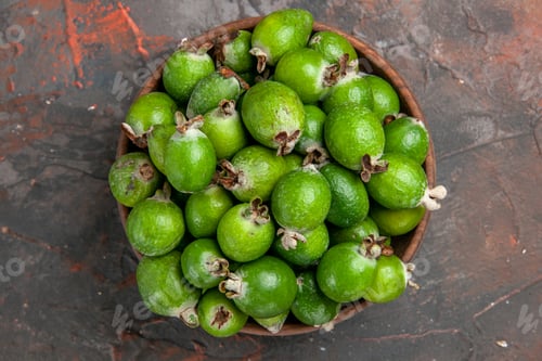 Preview: Overhead view of green small vitamin bomb fresh feijoas in a brown pot on mixed color background