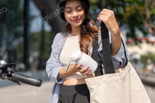 Preview: Close up asian woman putting thermos tumbler in eco bag while riding bicycle in park under sunlight