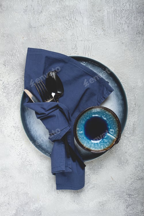 Preview: food background, with an empty blue plate, a bowl, black cutlery,with a napkin,on a gray background,