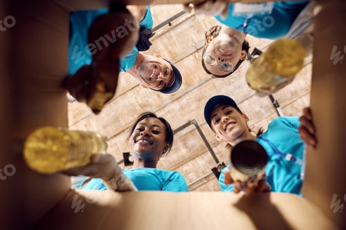 Preview: Below view of volunteers packing donated food in cardboard box.