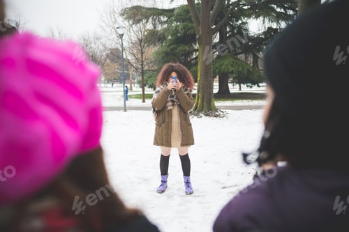 Preview: curly woman standing in park and using smartphone