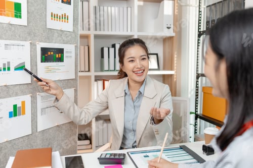 Preview: Two Asian businesswomen discussing company strategy together in a modern office