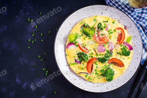 Preview: Omelette with broccoli, tomatoes and red onions on dark table.