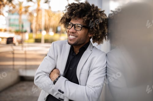 Preview: Excited african american middle aged businessman in suit posing with crossed arms, leaning on wall