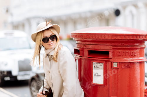 Preview: Stylish young woman waiting by red post box, London, England, UK
