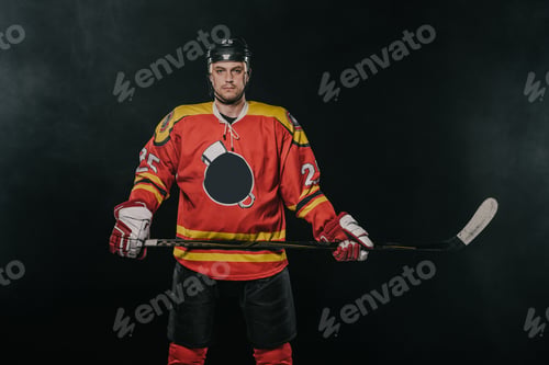 Preview: professional ice hockey player holding hockey stick and looking at camera isolated on black