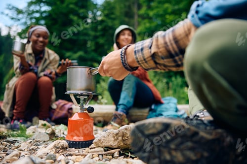 Preview: Close up of man making tea on portable stove while camping with friends in nature.