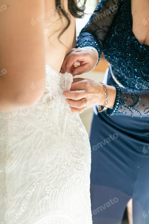 Preview: Mother of bride helping bride put on wedding dress