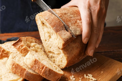 Preview: Woman cutting fresh bread at wooden table, closeup