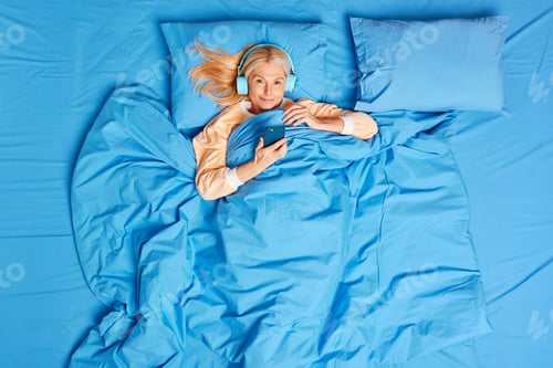 Preview: View from above of middle aged woman uses smartphone and stereo headphones for listening relaxing mu