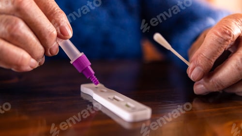 Preview: Close-up of caucasian grandma placing sample into buffer dropper for coronavirus
