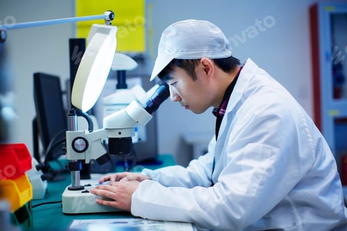 Preview: Workers at small parts manufacturing factory in China looking through microscope