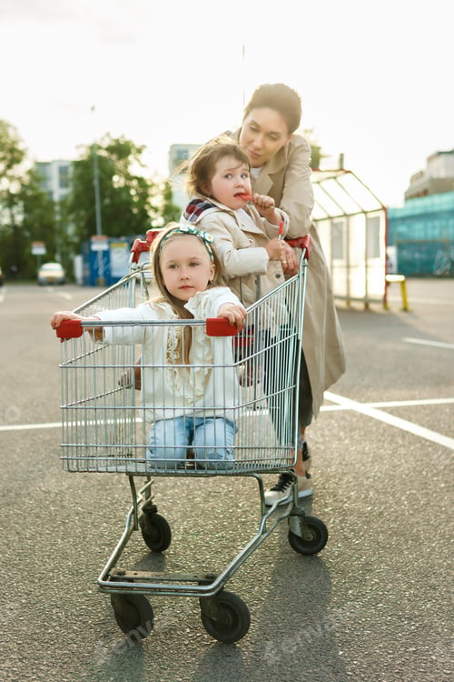 Preview: Happy mother and her daughters having fun with shopping cart on a parking lot beside a supermarket.