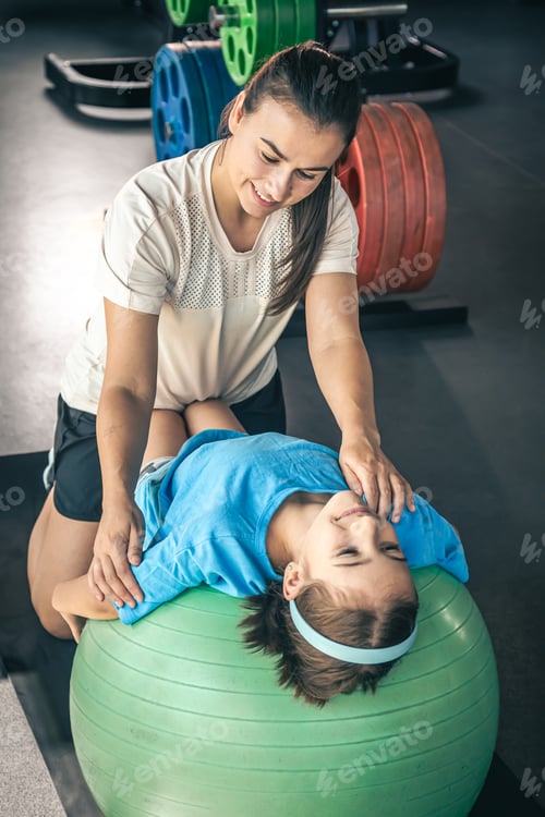 Preview: Cute child girl stretching on pilates fitness ball with mom in gym.
