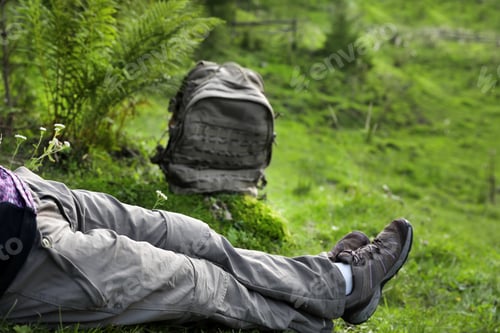 Preview: Woman with backpack sitting on green grass, closeup. Summer camping