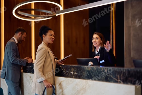 Preview: Happy hotel manager talking to African American businesswoman at reception desk.