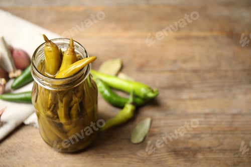 Preview: Glass jar with pickled peppers on wooden table. Space for text