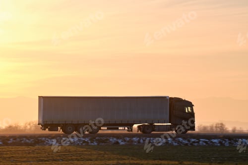 Preview: Semi-truck with cargo trailer driving on highway hauling goods in evening.