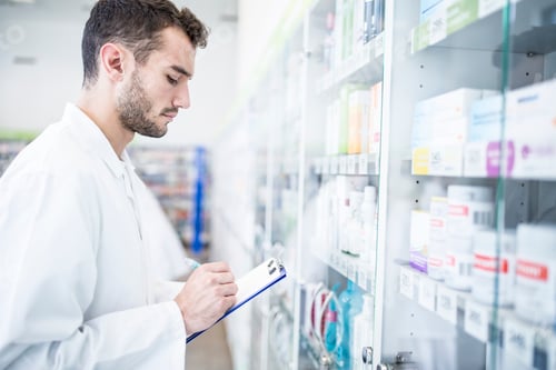 Preview: Pharmacist holding clipboard at shelf in pharmacy