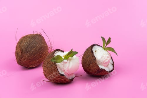 Preview: Vanilla ice cream balls in fresh coconut halves decorated with mint leaves on a pink background