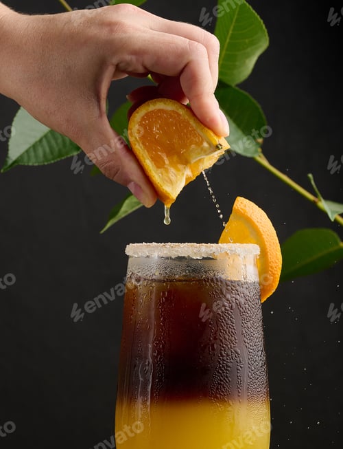 Visualização: Café gelado com suco de laranja em um copo transparente, a mão de uma mulher aperta uma fatia de laranja