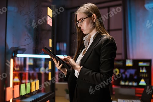 Preview: Businesswoman standing near glass office wall, using tablet computer